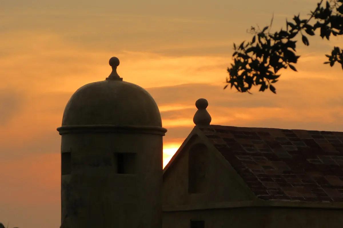 A small stone sentry box on a fort wall silhouetted against an orange sunset sky.