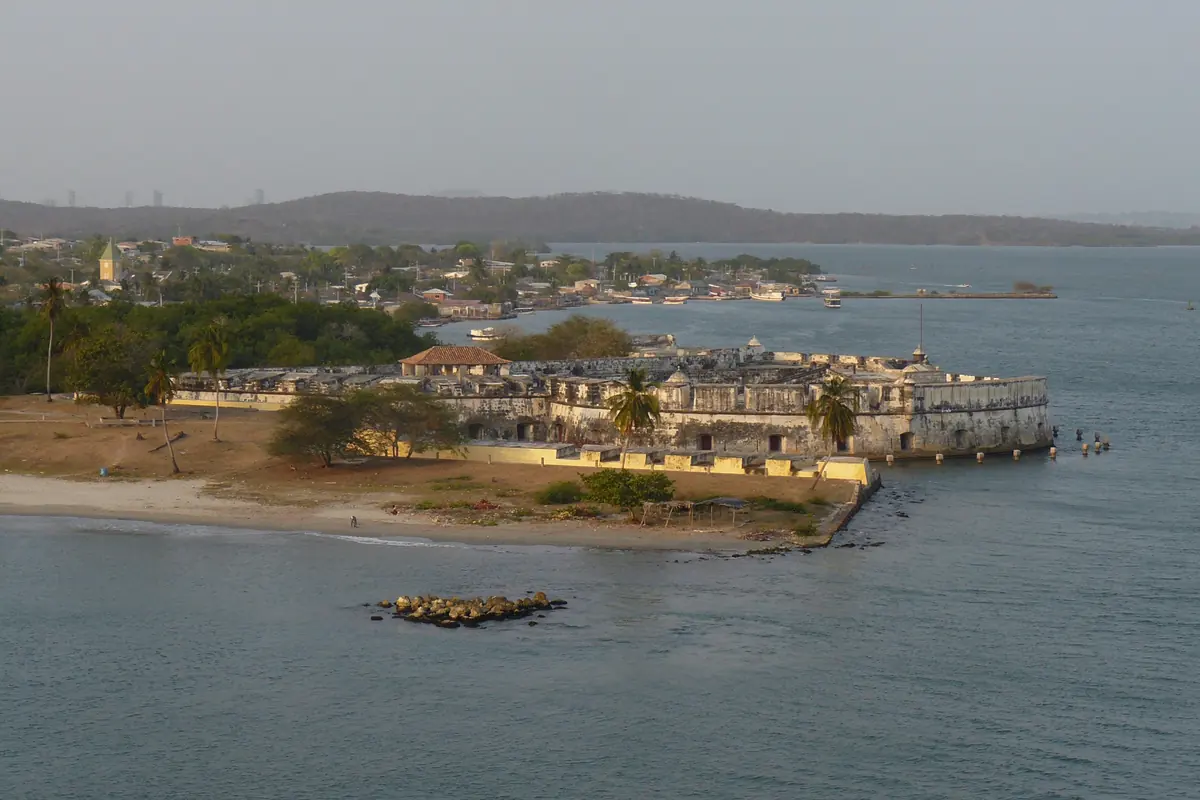 A coastal fort with low walls beside a beach and calm water, under a grey sky